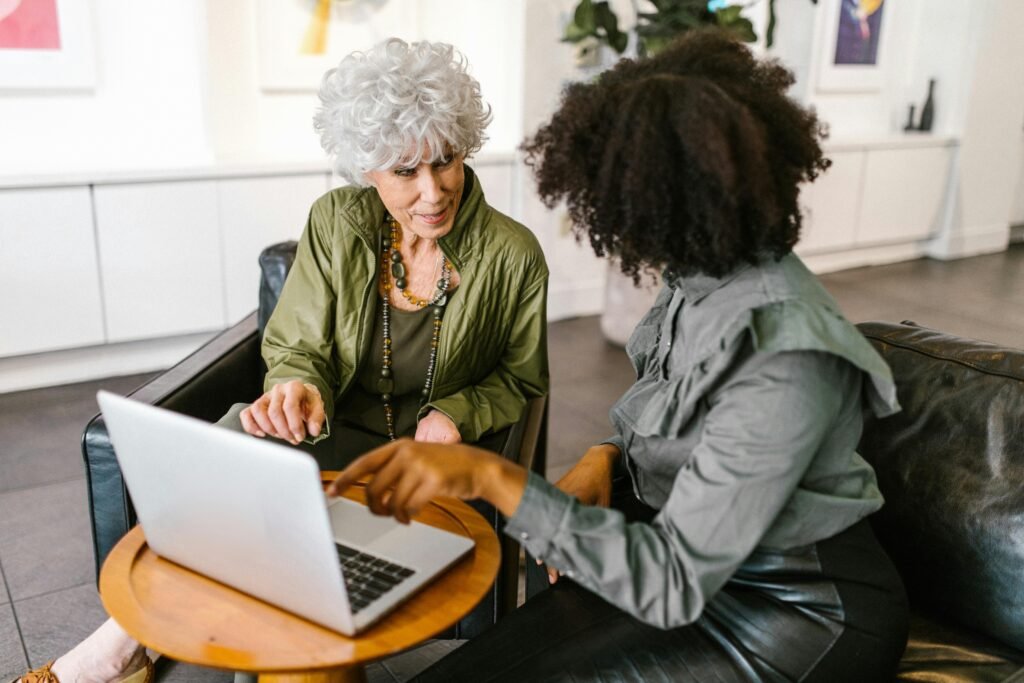 Two women discussing work on a laptop in a modern office setting.